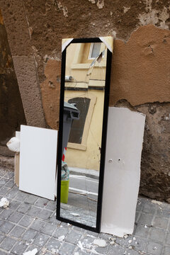 Broken mirror and other furniture items on street with reflection