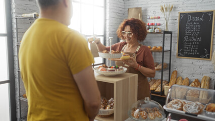 Woman baker serving a man customer in a cozy bakery with various pastries on display and a bread price list on the wall