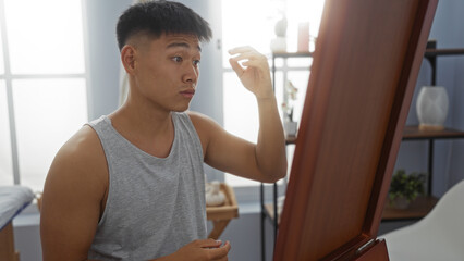 Young chinese man in a spa salon adjusting hair in front of a mirror in a wellness room