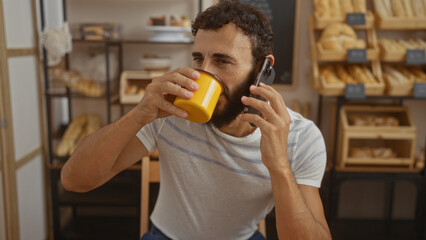Young man with beard drinking coffee and talking on phone in cozy bakery shop