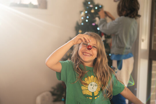 Kids decorating a Xmas tree; a child using a red bobble as a red nose