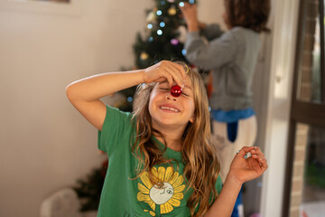 Kids decorating the Xmas tree, a child using a red bobble as red nose