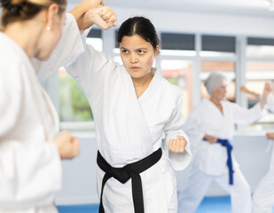 Experienced young Asian female karateka in kimono with black belt engaging kumite with rival,...