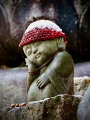 Snow-covered Jizo statue wearing a red knitted hat on Mount Miyajima, Japan, symbolizing protection.