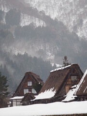 Traditional Gassho-style houses in Shirakawa-go, Japan, covered in snow with misty mountains in the background.