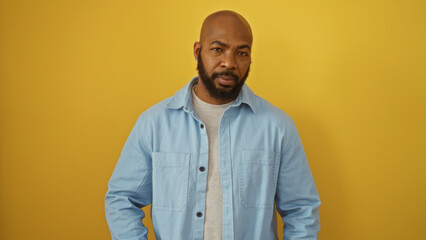 Handsome young african american man with a beard standing against a vibrant yellow background