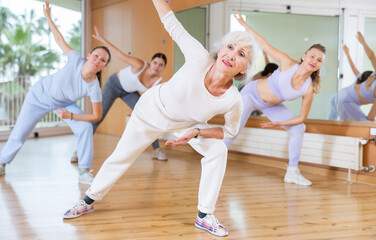 Obraz premium Active positive senior woman performing dance elements during lesson with female group in modern school for adults