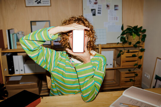 Designer hiding face with smartphone in office