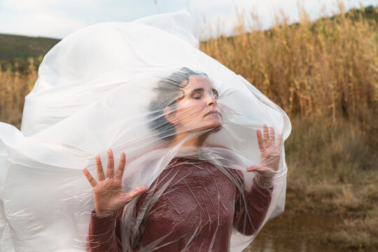 Young woman trying to breathe in plastic sheet blowing in the wind