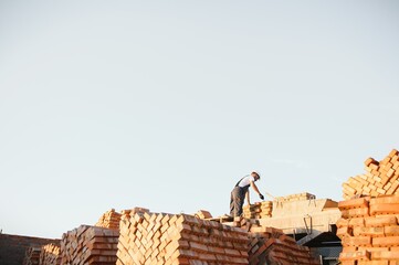 construction mason worker bricklayer installing red brick with trowel putty knife outdoors