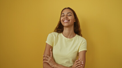 Obraz premium Young woman with arms crossed smiling against isolated yellow background