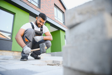 Indian Worker skillfully laying paving stones using a hammer and wearing gloves, showcasing...