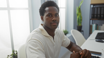 Handsome young man working in an office setting with a computer on the desk and books on the shelves behind him, showcasing a professional workspace indoors