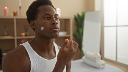Attractive man in a spa applying skincare product to his face, sitting in a serene wellness center with candles and soft lighting