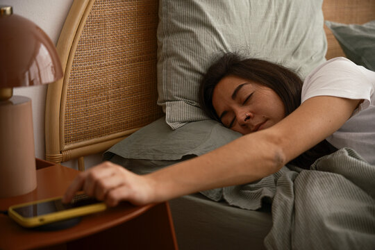 Sleepy woman turning off alarm on smartphone in morning