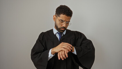 Handsome young man in graduation gown and glasses checking watch against white background