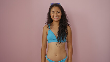 Young chinese woman in a blue bikini smiling against an isolated pink background