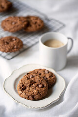 Double Dark Chocolate Cookies with coffee espresso cup, cooling rack and plate on a white background