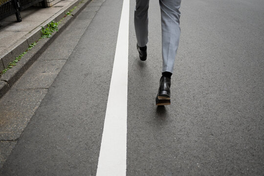 Businessperson walking along white road markings on asphalt