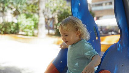Blonde toddler boy playing on a colorful playground in an urban park, showcasing an adorable childhood moment.