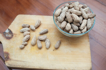 Organic Raw Peanuts in a glass Bowl on wooden cutting board in the wooden table, healthy snack
