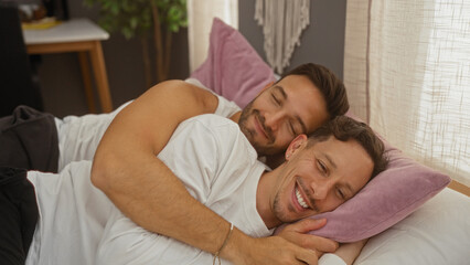 Two men in a loving embrace on a bed in a cozy bedroom showcase their bond and happiness, highlighting themes of gay, lgbt, family, and home.