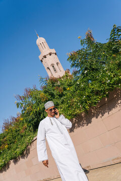 Omani man talking on phone walking near sultan qaboos grand mosque