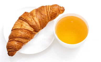 A golden croissant served on a white plate next to a cup of warm tea