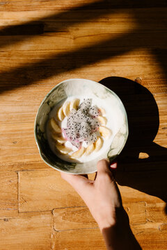 Unknown hand placing a yogurt bowl with banana and pitahaya on a table