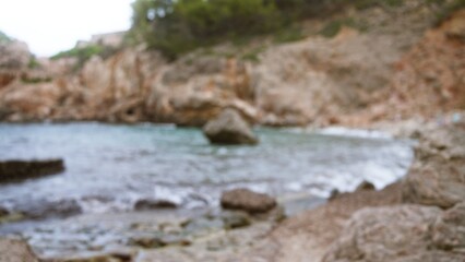 Blurred background of rocky coastal scene in mallorca, spain with out-of-focus ocean and cliffs under defocused sky, capturing an outdoor natural bokeh landscape.