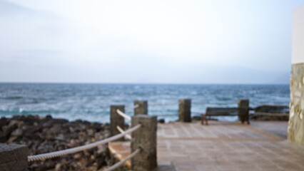 Blurry ocean view with bokeh effect in lanzarote, spain showcasing an outdoor terrace near the atlantic ocean in the canary islands with a defocused stone railing and bench.