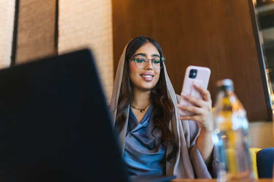 Smiling muslim businesswoman using laptop and smartphone in a cafe