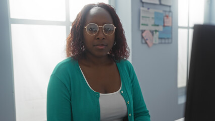 Woman working in office wearing glasses and green sweater focusing on computer screen