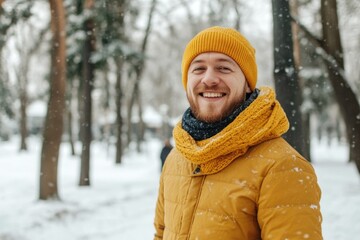 Obraz premium With a warm smile, a stylish man in a vibrant yellow coat and matching beanie walks through a snowy park, embodying youthful winter fashion and cheerful vibes