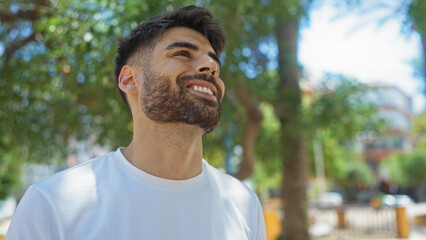 Handsome man smiling outdoors in urban park setting with trees in the background