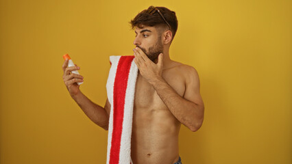 Handsome young man with a beard looks surprised at a bottle while covering his mouth with his hand,...