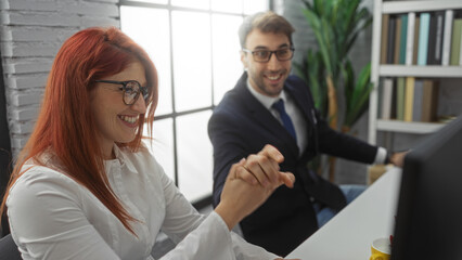 Obraz premium Hispanic business partners, a man and woman, celebrate success in a bright office, shaking hands in agreement while smiling enthusiastically in a professional setting.