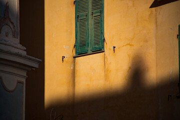 Sunlight casting shadows on a vibrant yellow wall with green shutters