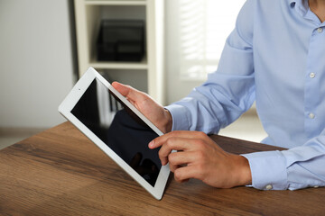 Businessman using tablet at wooden table, closeup. Modern technology