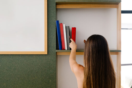 Woman taking a book from a bookshelf in the living room of her house