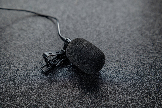 Compact coloured tie clip microphone for interviews with pop filter on black glossy background. Concept: Audio, professional sound, sound.