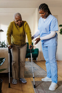 Nurse assisting elderly woman using crutches at home