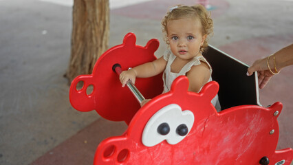 Toddler girl enjoying a playful ride on a red toy at an outdoor playground in the park, showcasing her cute and adorable childhood moments.