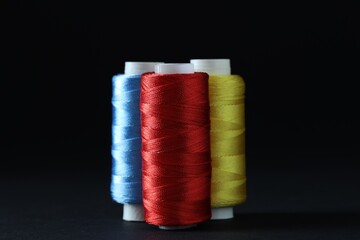 Spools of colorful sewing threads on black background