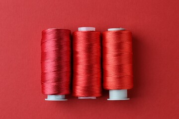 Spools of colorful sewing threads on red background, flat lay