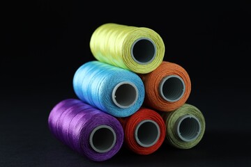 Spools of colorful sewing threads on black background, closeup
