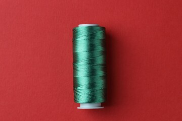 Spool of green sewing thread on red background, top view