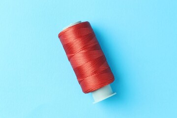 Spool of red sewing thread on light blue background, top view