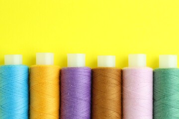 Spools of colorful sewing threads on yellow background, flat lay. Space for text