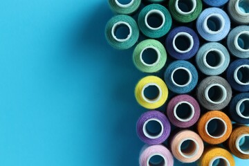 Spools of colorful sewing threads on light blue background, flat lay. Space for text